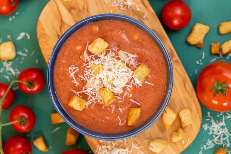An overhead shot of 3-ingredient white bean tomato soup in a blue bowl on a cutting board, topped with croutons and parmesan cheese.
