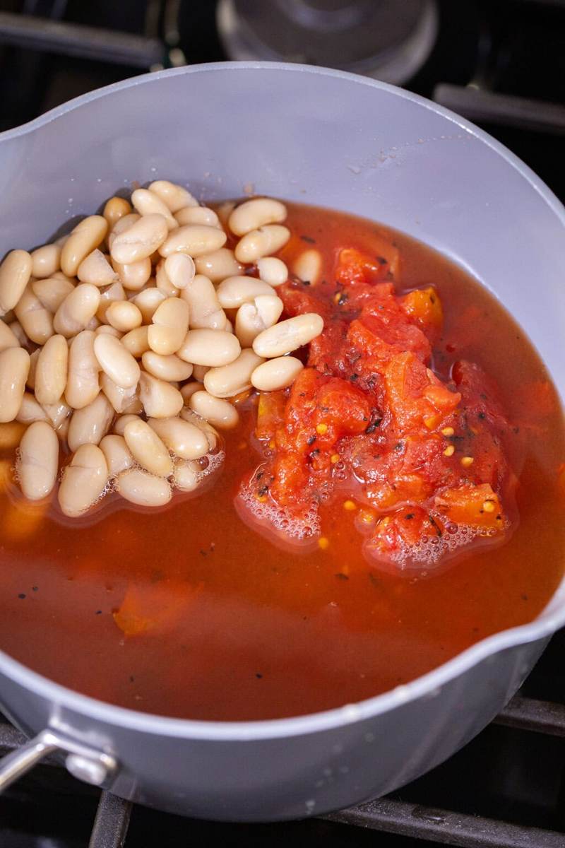 Crushed tomatoes, cannellini beans, and vegetable broth being added to a pot to make 3-ingredient white bean tomato soup.