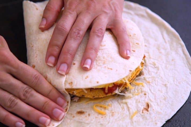 Place a small tortilla circle on top of cheese, then begin folding up edges of the large tortilla.