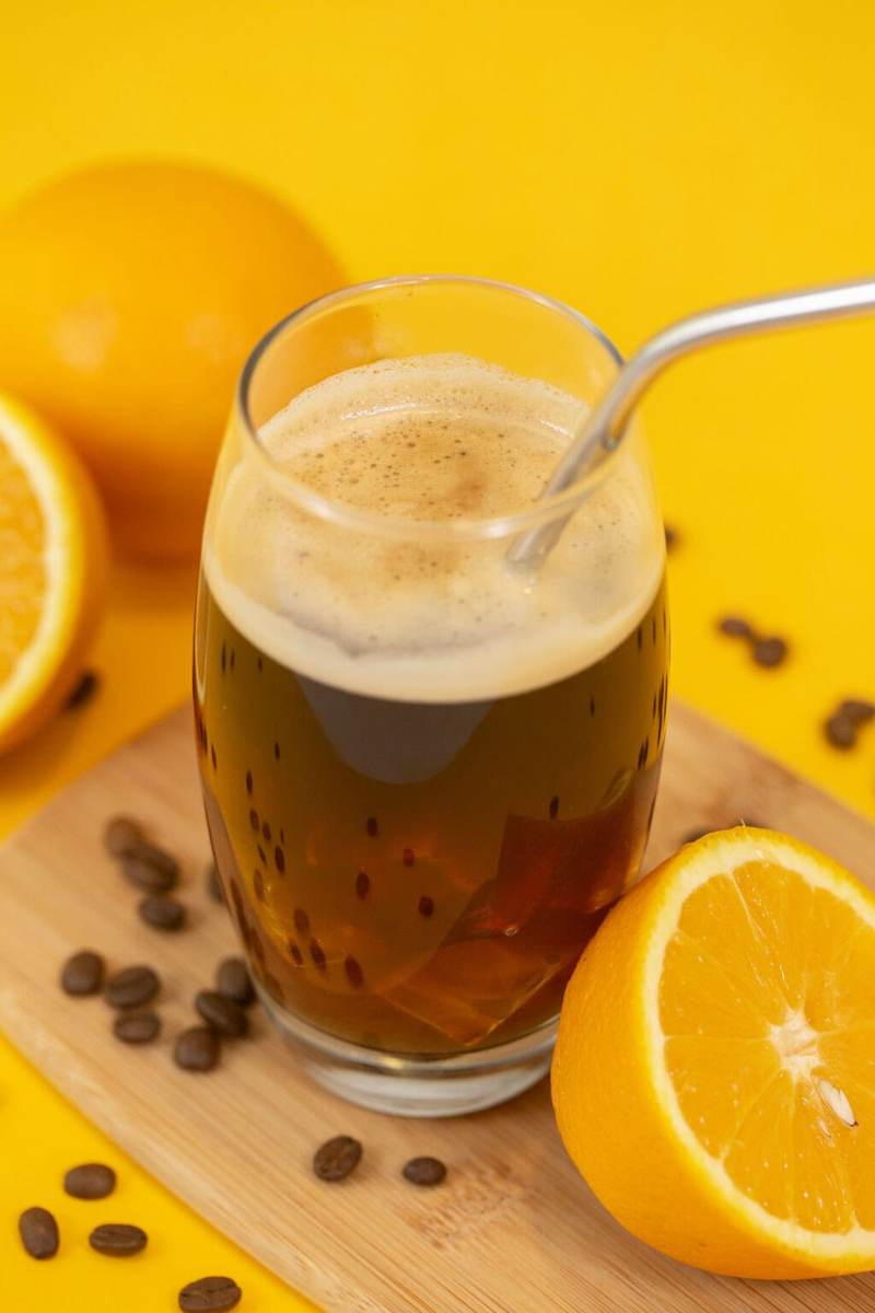 Another photo of the americano on a yellow table next to a sliced orange
