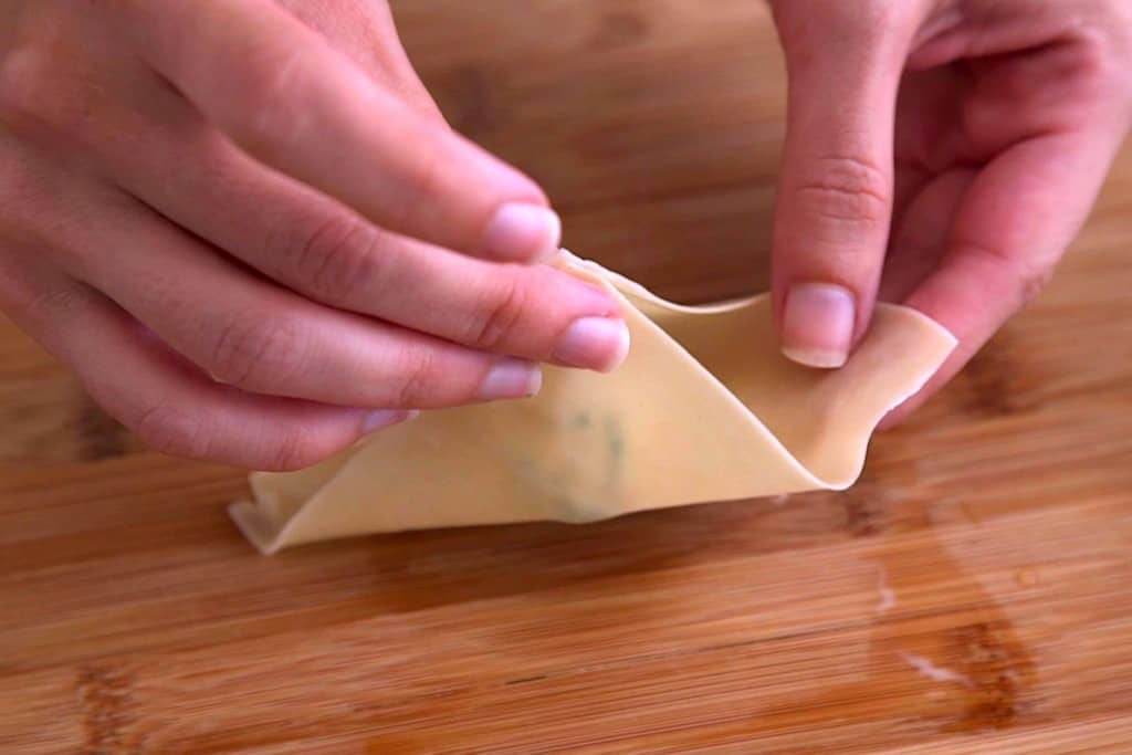 How to fold crab rangoon, folding opposite corners of wonton wrapper together to form a purse shape.