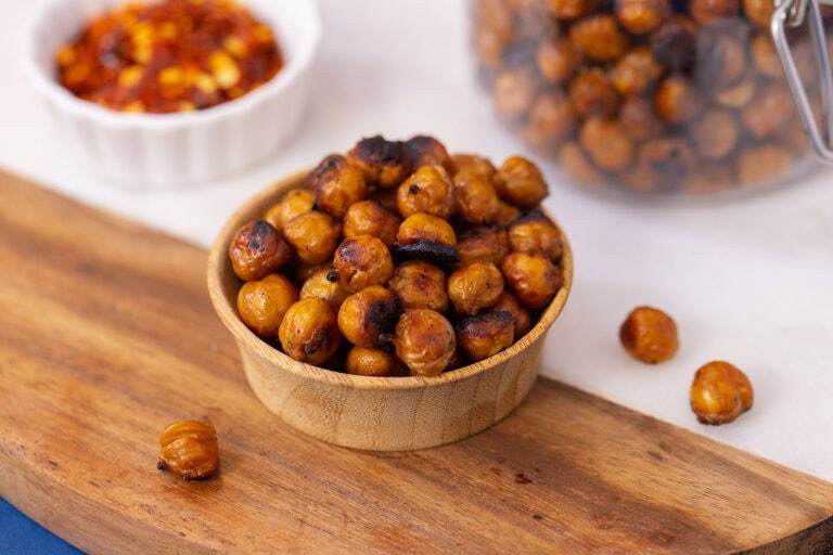 Top-down view of a bowl packed with crispy roasted chickpeas and a small bowl of chili flakes nearby.