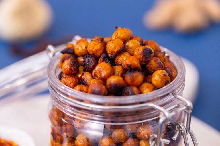 Glass jar filled with crunchy Asian-style roasted chickpeas on a white cutting board on a blue table.