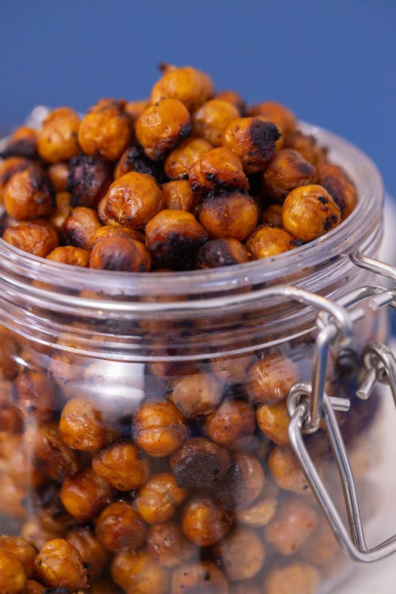 Glass jar filled with crunchy Asian-style roasted chickpeas on a blue table.