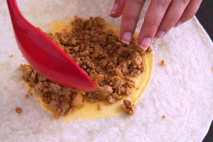 Spread nacho cheese sauce in the middle of each large tortilla, leaving room around the edges, and then begin to layer on meat and additional fillings.