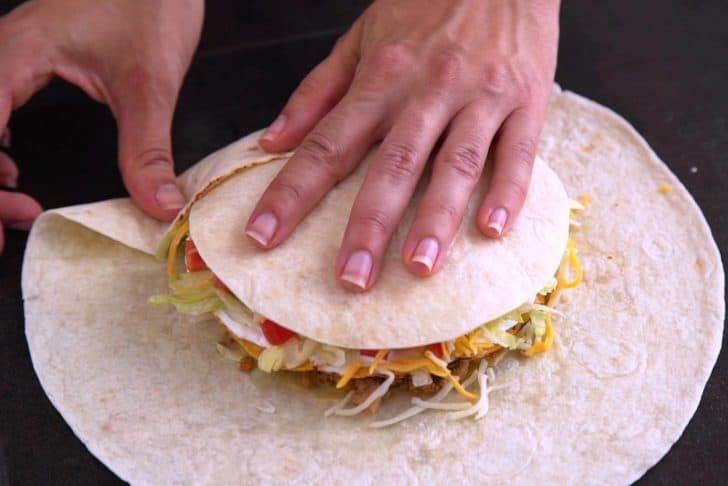 Place small tortilla circle on top of cheese and begin to fold up the edges of the large tortilla.
