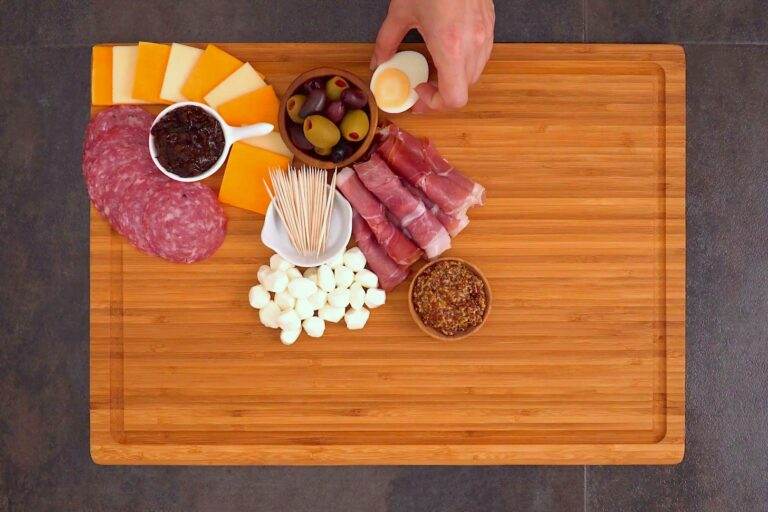 First, add dip bowls to your charcuterie board. Then build around the bowls with your meats & cheeses.