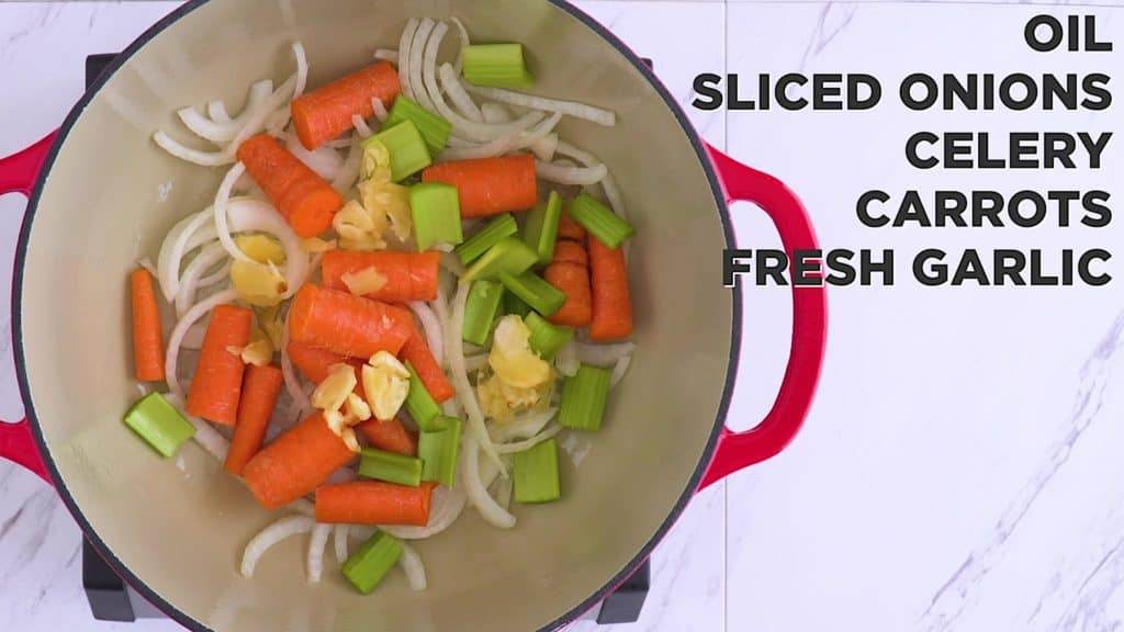 Adding garlic, onion, carrots and celery to a pot.