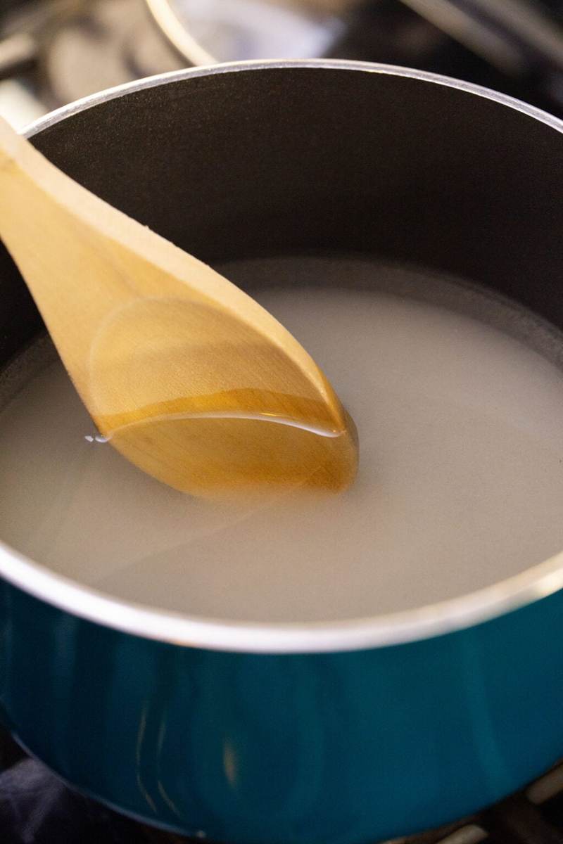 Using a wooden spoon to stir sugar and water in a pot over the stove.
