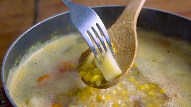 Using a fork to remove a chunk of potato from the boiling vegetables to test the potatoes and make sure they're cooked through.