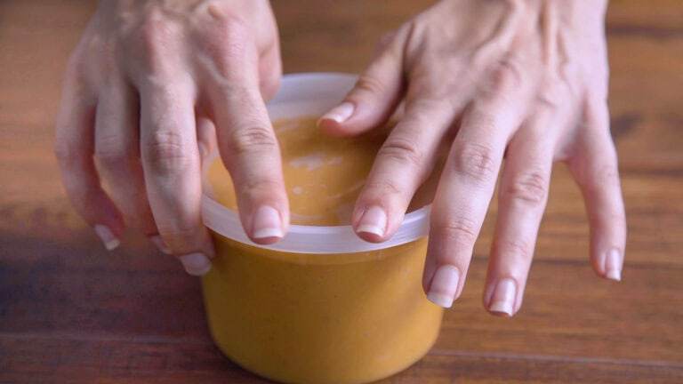 closing a meal prep container filled with soup to store for later.