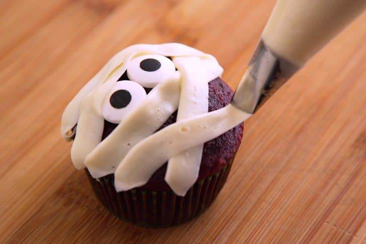 Stick candy eyes onto cupcake. Add white frosting into a decorating bag with a petal piping tip, then draw horizontal stripes as mummy 'wrapping.'