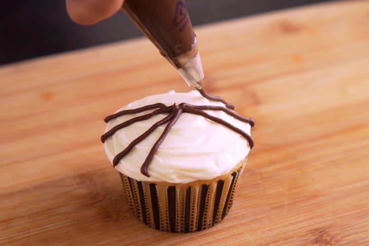 Using chocolate frosting and a small round piping tip (or black decorating gel), draw 8 spider legs onto each cupcake—starting from the outside and meeting in the middle.