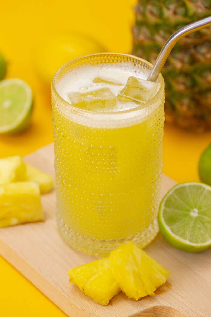 Pineapple agua fresca in a glass, sitting on a cutting board surrounded by ingredients.