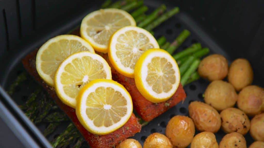 Jerk Salmon being placed into the Air Fryer with asparagus and potatoes, topped with lemon slices.
