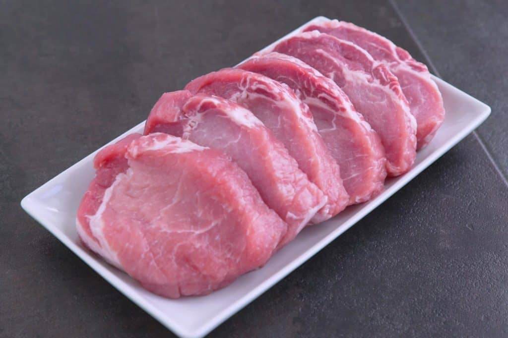 Fresh raw pork chops on a white plate.