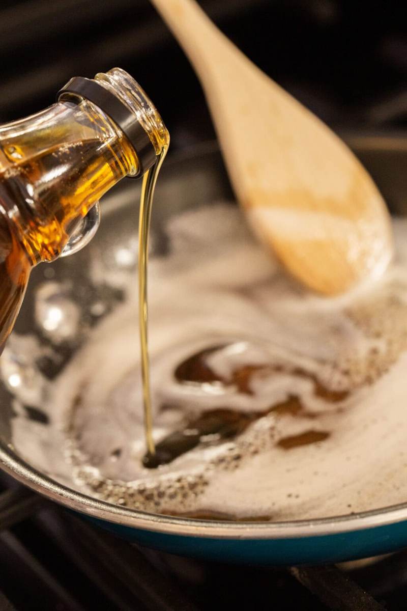 A pan on the stove filled with melting butter. Maple syrup is being poured into the pan.