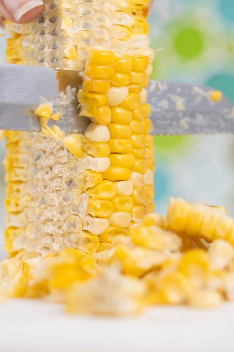 A photo of using a small serrated knife to carefully slice the corn off of the cob so as to keep it held together in chunks rather than individual kernels.