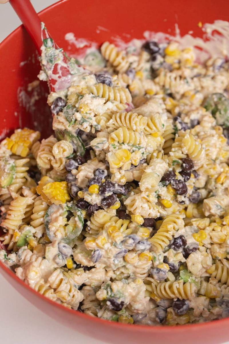 using a large silicon spatula to finally mix all the ingredients of her Easy Mexican Street Corn Pasta Salad together.