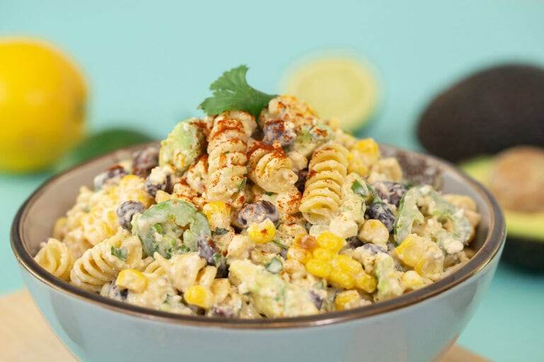 Another side profile shot of the Mexican Street Corn Pasta Salad, again on a blue table surrounded with ingredients.