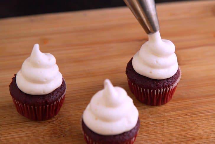 Add marshmallow frosting into a decorating bag with a large round piping tip. Squeeze frosting onto cooled mini cupcakes in a rising spiral pattern, creating little ghost poofs.