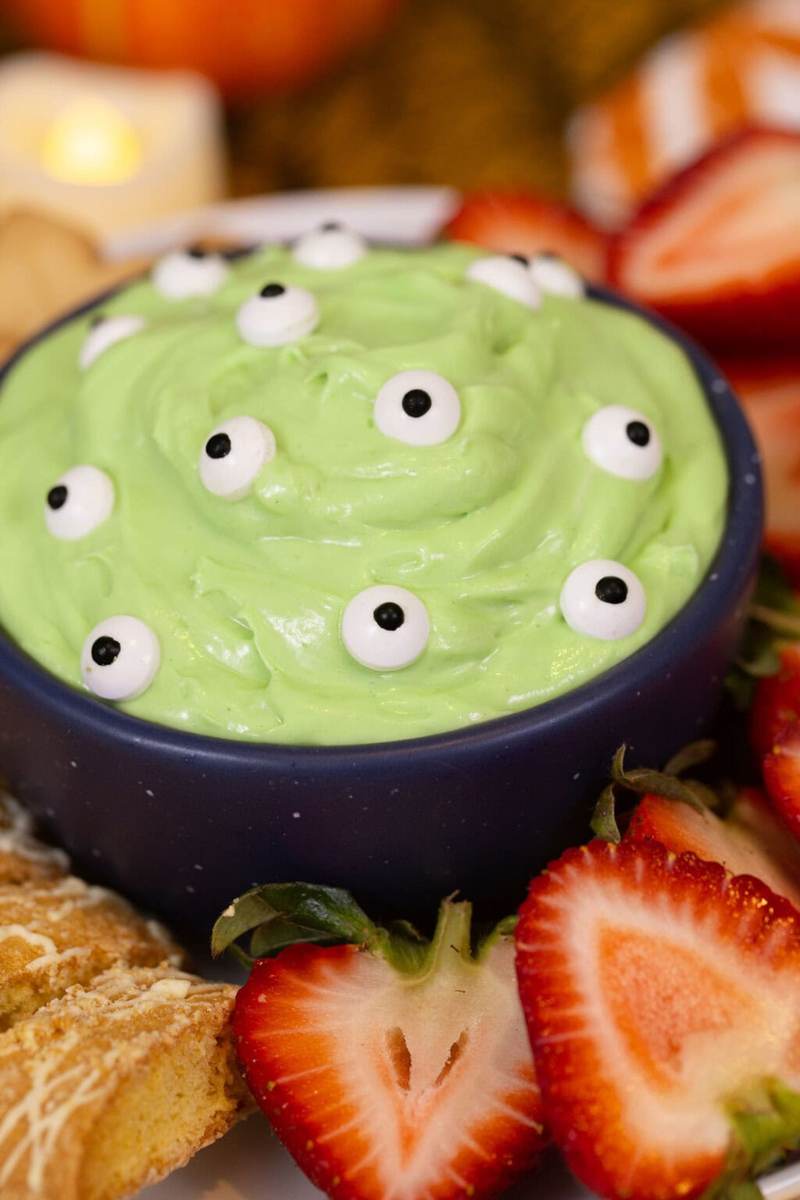 An image of green monster marshmallow dip, covered with candy eyes and surrounded by dippers.