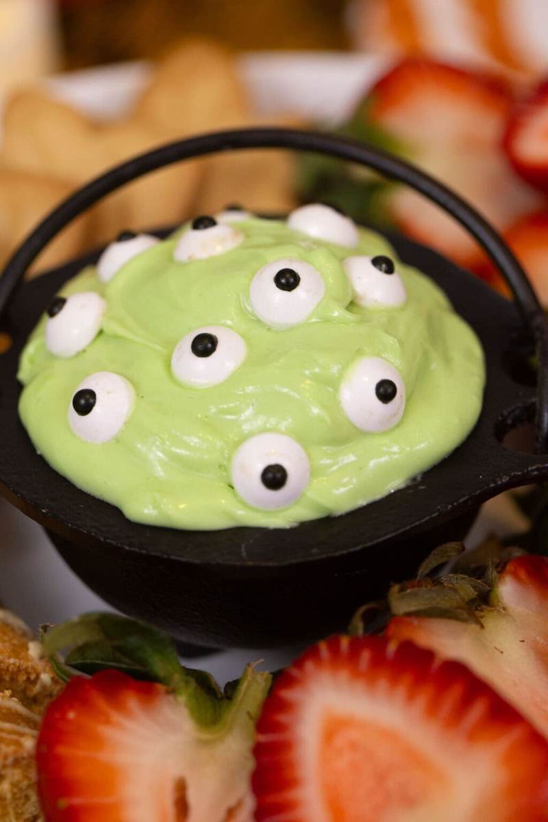 A miniature cauldron bowl filled with green marshmallow dip dotted with candy eyes