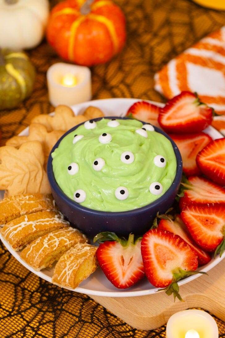 An image of green monster marshmallow dip, covered with candy eyes and surrounded by dippers.