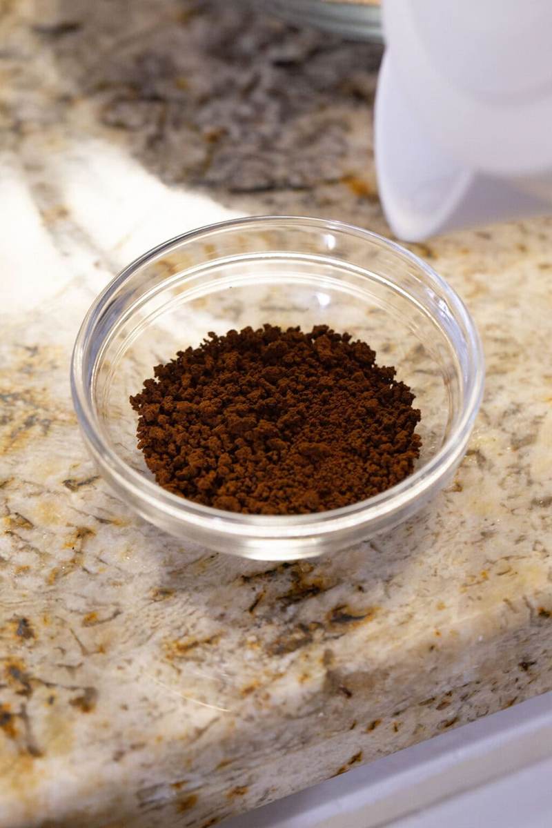 A small duralex bowl filled with instant coffee, an electric kettle about to pour hot water into the bowl.