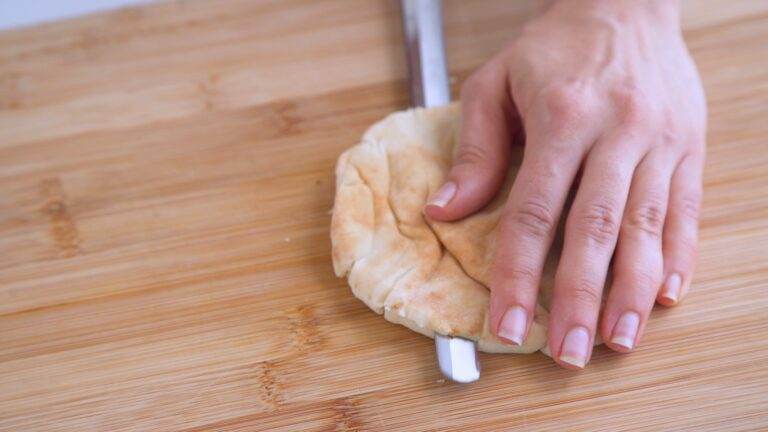 Using a serrated knife to cut the pita pockets into halves.