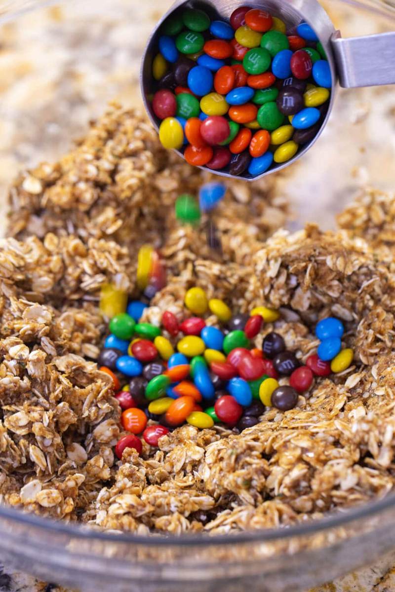 Using a measuring cup to add mini M&Ms to the protein ball oat mixture.