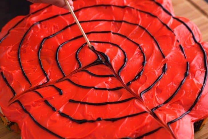 Use black decorating gel to draw a large black dot in the middle, surrounded by 4-5 concentric circles. Then, use a wooden skewer to drag black gel from the center dot out to the edges in straight lines, creating a web effect.