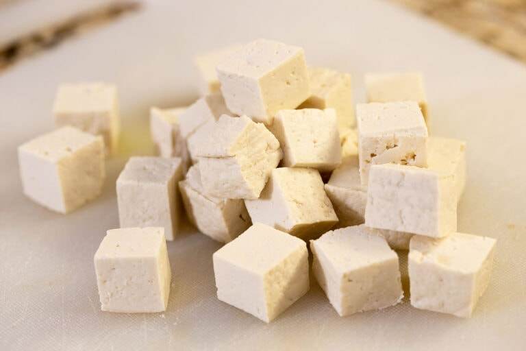 A pile of uncooked tofu cubes, just pressed and dry, on a white cutting board.