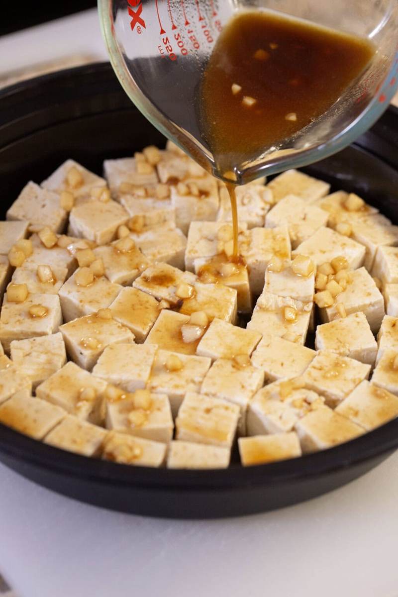 A black bowl with uncooked tofu being marinated in a sesame ginger sauce.