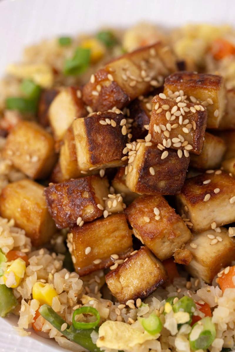 A white bowl with cauliflower fried rice, topped with sesame ginger tofu and sesame seeds.