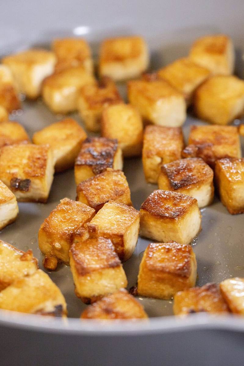 A gray pan on the stove, inside are crispy sesame ginger tofu cubes.