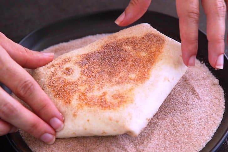Upon finishing cooking, spray smores crunchwrap lightly with cooking spray and gently toss in cinnamon sugar to coat.