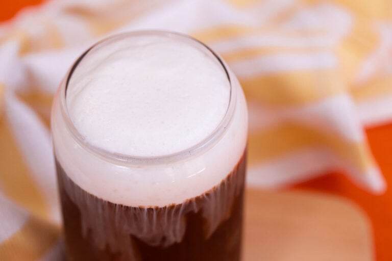 Iced coffee in a glass with vanilla sweet cream cold foam on a wooden cutting board.