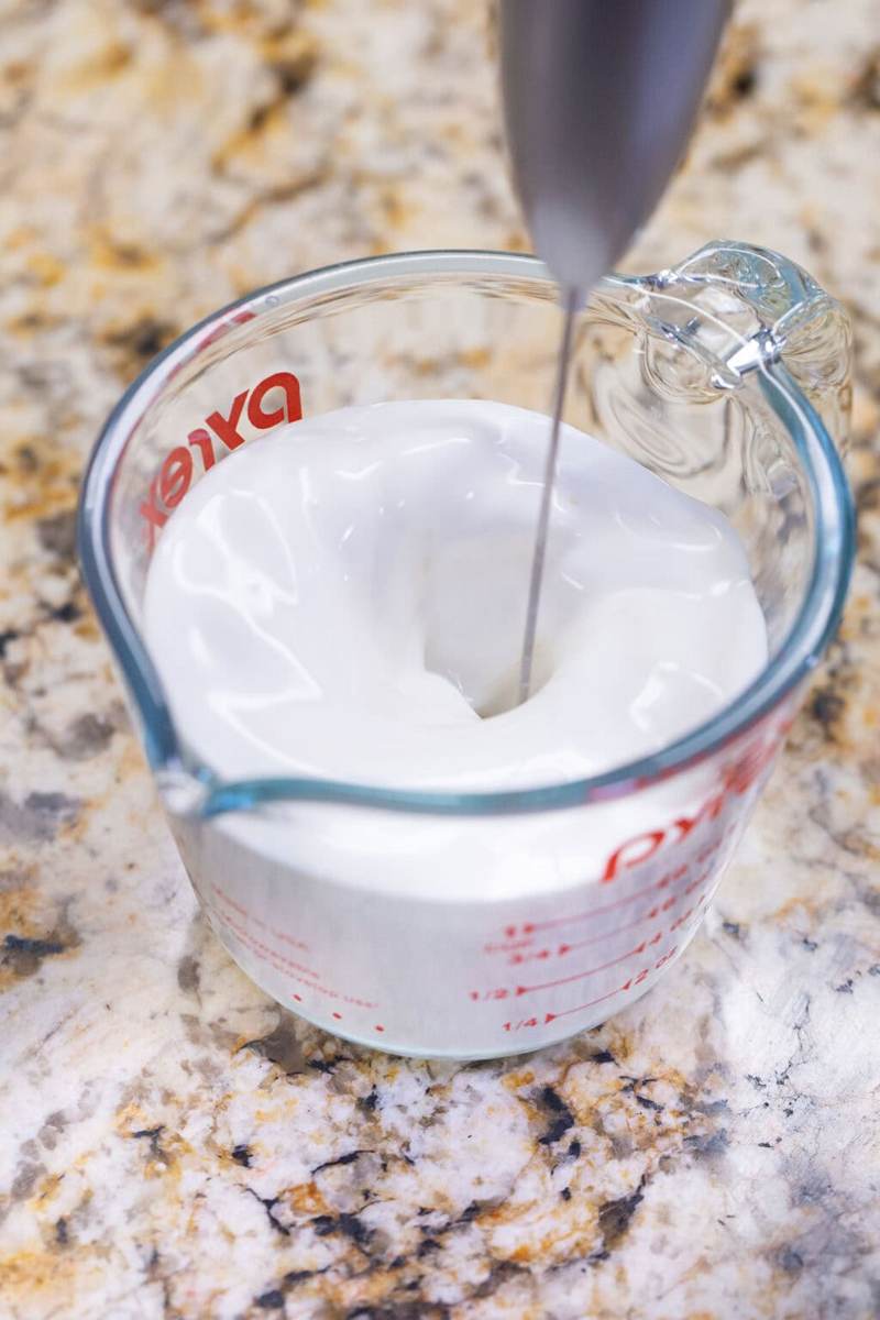 using a hand frother to whip up the vanilla sweet cream cold foam in a glass measuring cup.