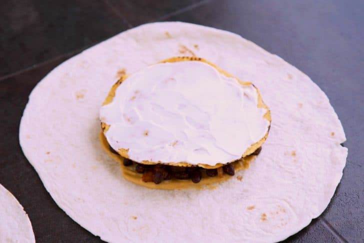 Spread vegan sour cream onto corn tostada and place on top of beans.