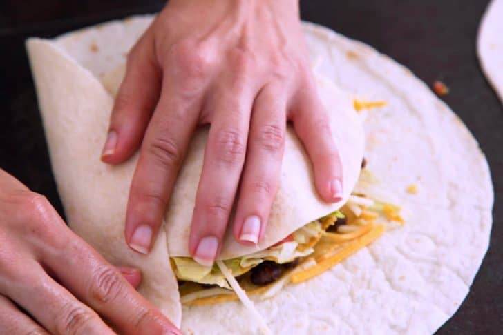 Place a small tortilla circle on top, then begin folding in the edges of the large tortilla.