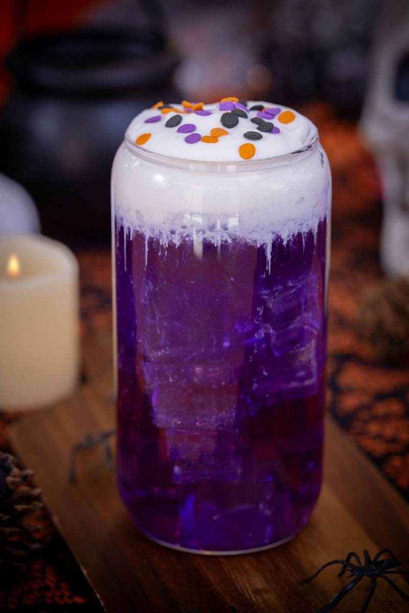 A purple, halloween themed witch's brew dirty soda on a table with halloween decorations