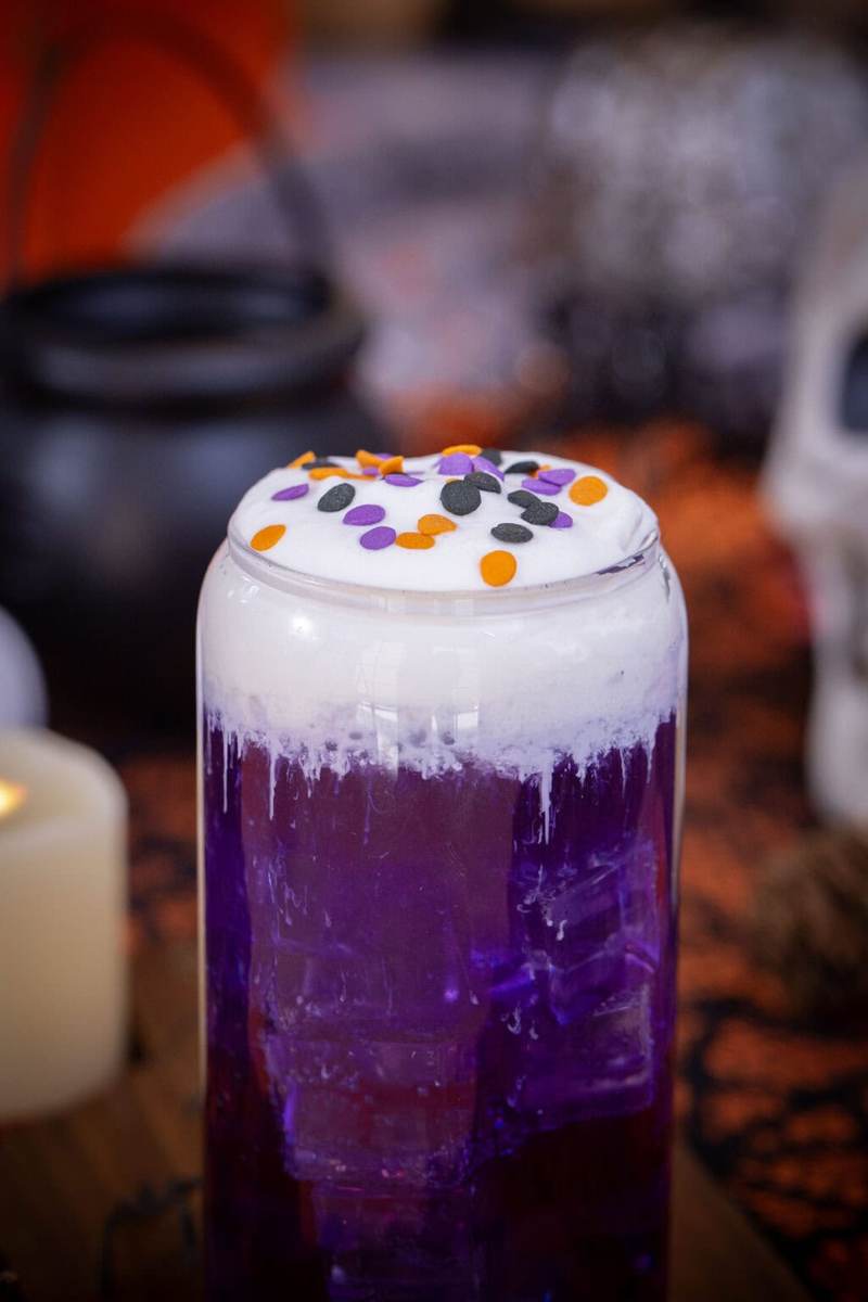 A close up shot of a purple halloween themed witch's brew dirty soda on a table with halloween decorations