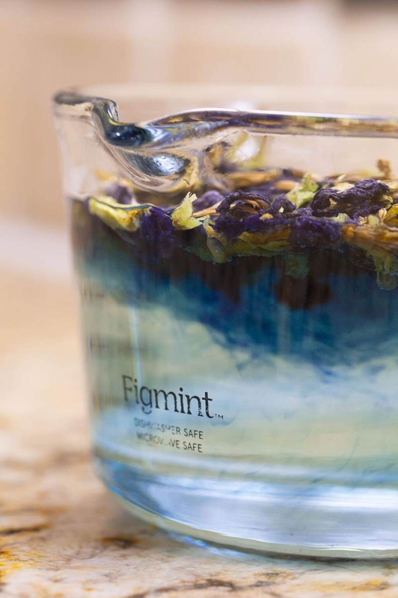A glass measuring cup filled with hot water and steeping butterfly pea tea leaves, the blue color of the tea beginning to show.