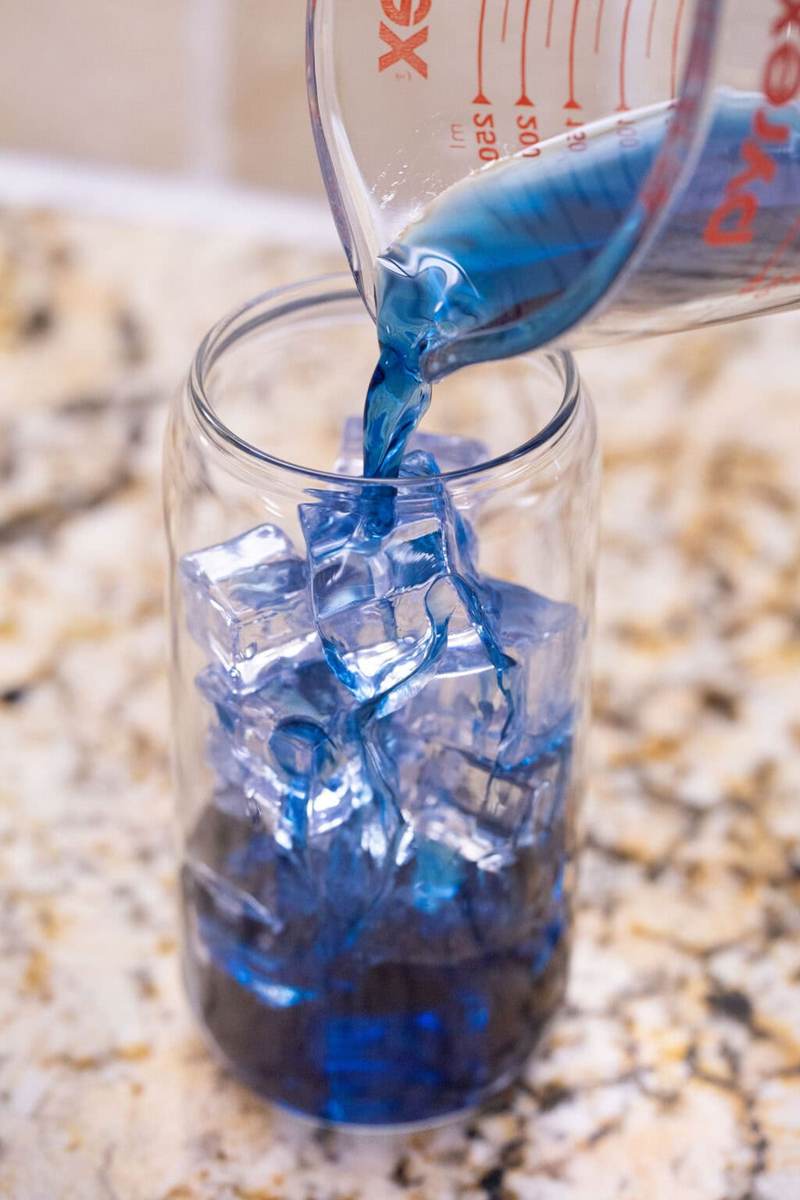 Pouring butterfly pea tea into a glass with ice.